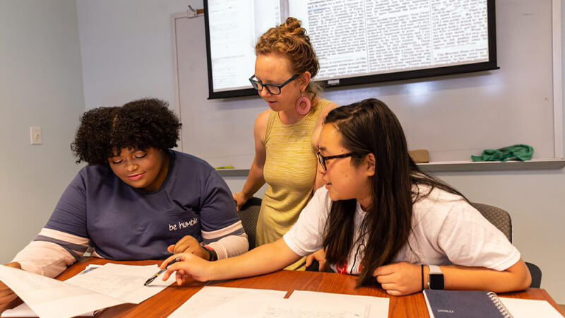 Two students review documents with a professor