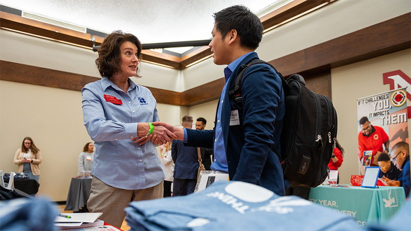 Student shaking hand with faculty member at an academic fair.