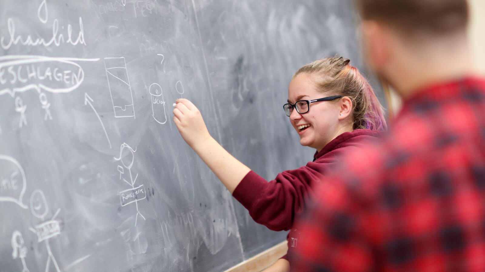 Woman at chalkboard writing in German.