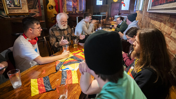 People talk while seated around a table decked with German flags.